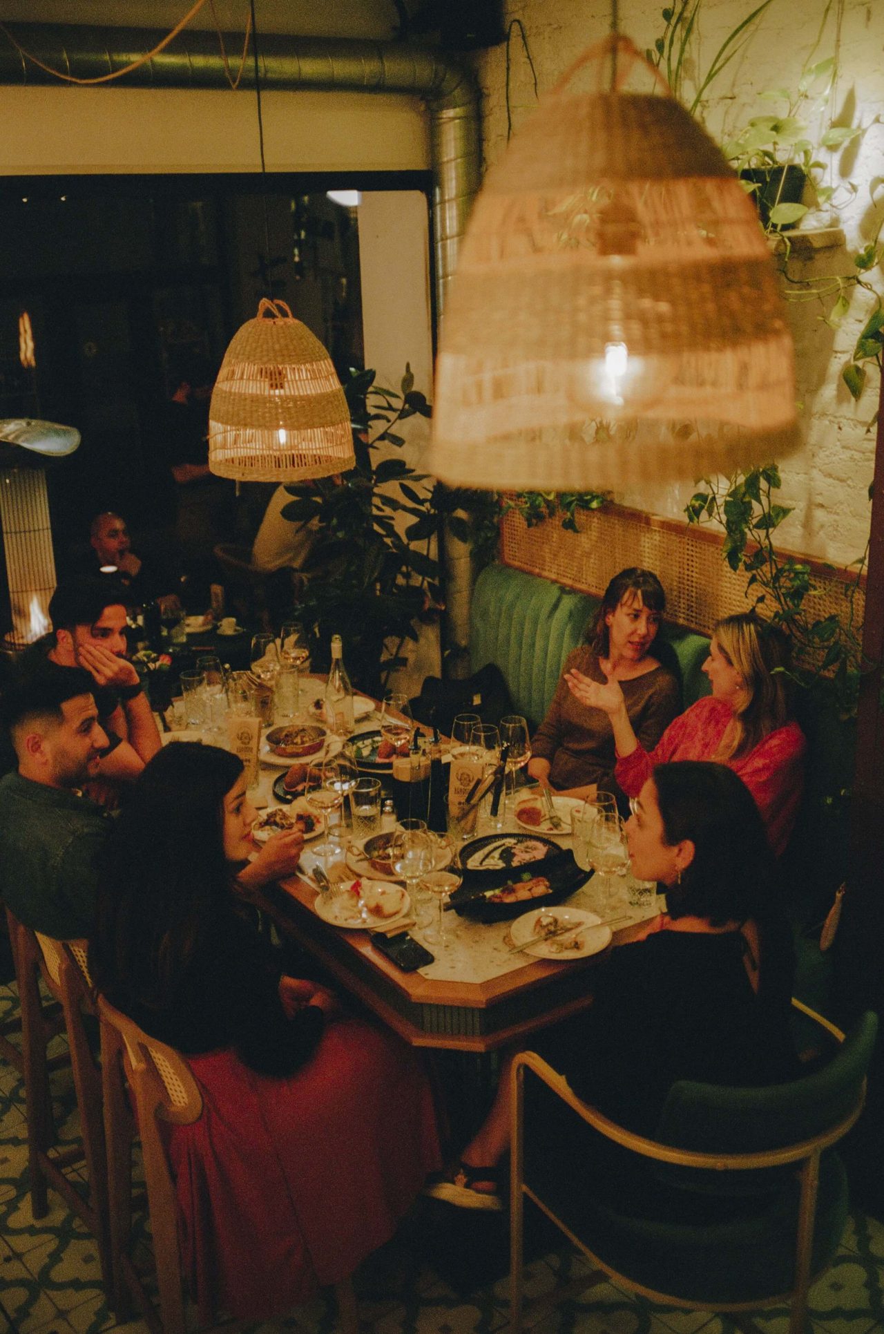A group of people sit and converse at a restraurant table covered in food